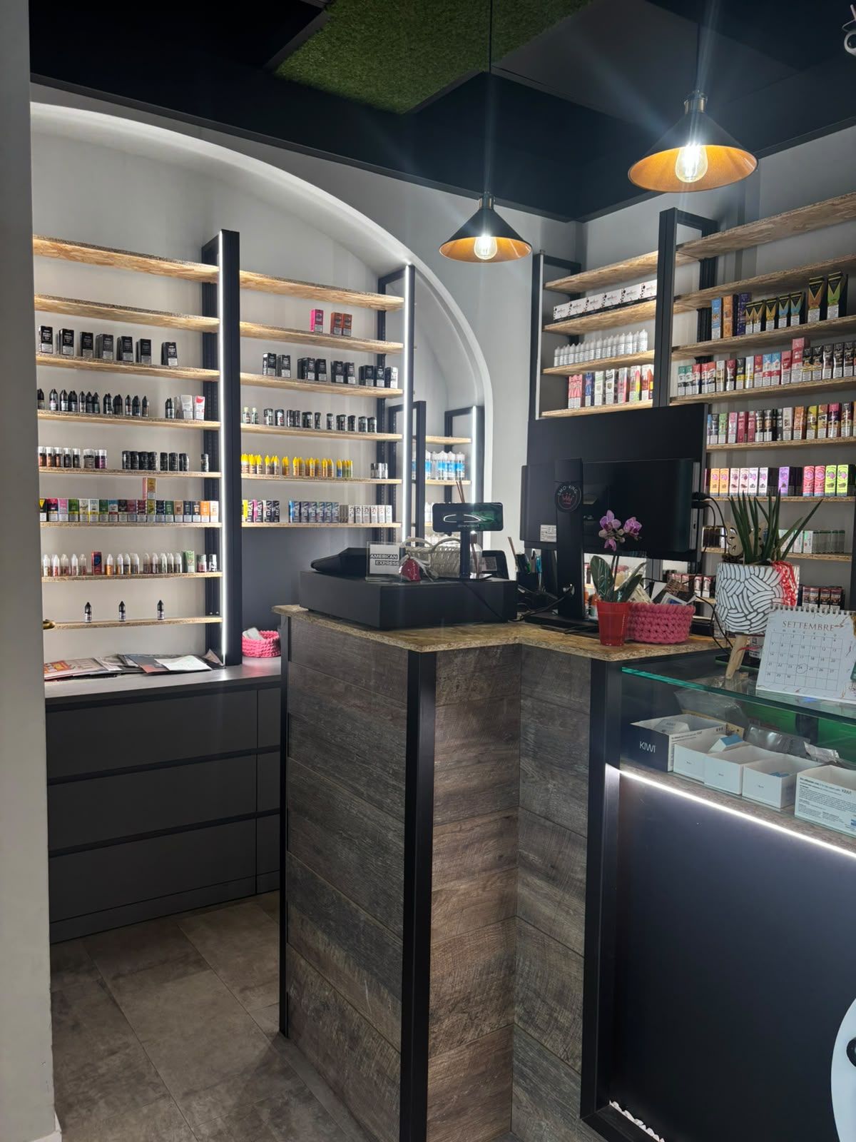 Interno del negozio Smo-King Vape Domus di Prati con bancone, lampade a sospensione e scaffali di liquidi